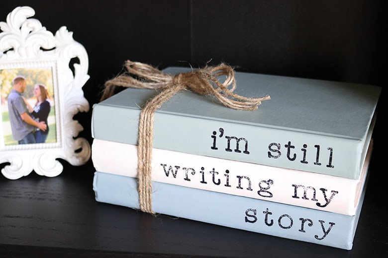 Painted books with sayings are a super easy addition to your home decor! This DIY with chalk paint and acrylic stamps is a thrifty way to use old books. Display them on shelves, use for a wedding, or lay them on a coffee table. Learn how to make them with this tutorial! 