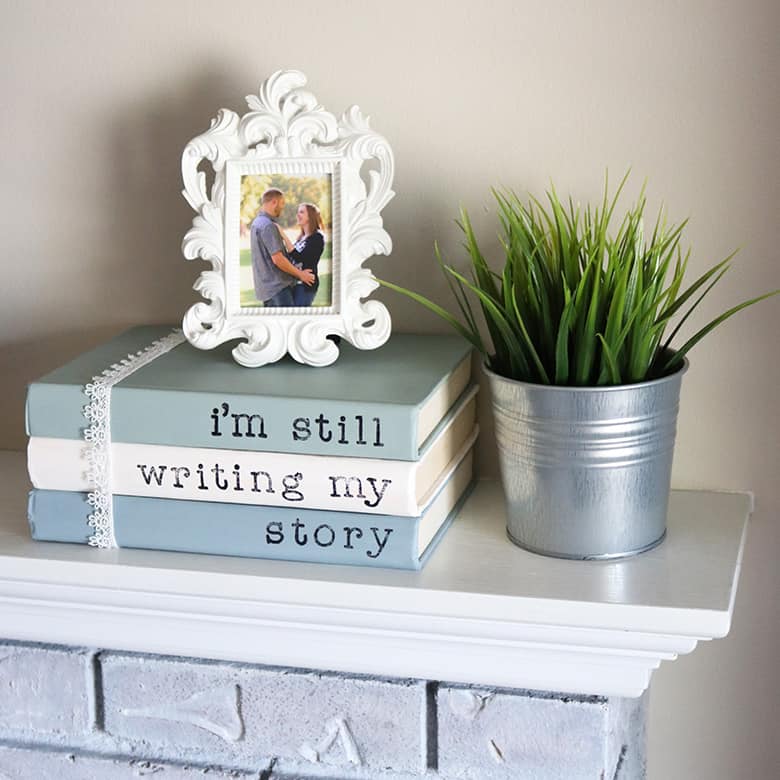 Painted books with sayings are a super easy addition to your home decor! This DIY with chalk paint and acrylic stamps is a thrifty way to use old books. Display them on shelves, use for a wedding, or lay them on a coffee table. Learn how to make them with this tutorial!