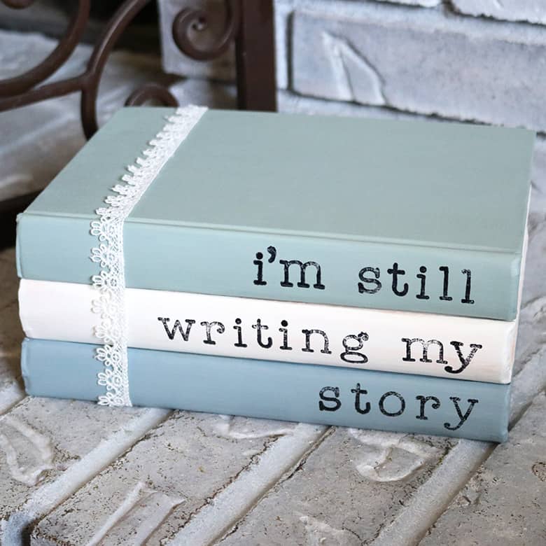 Painted books with sayings are a super easy addition to your home decor! This DIY with chalk paint and acrylic stamps is a thrifty way to use old books. Display them on shelves, use for a wedding, or lay them on a coffee table. Learn how to make them with this tutorial!