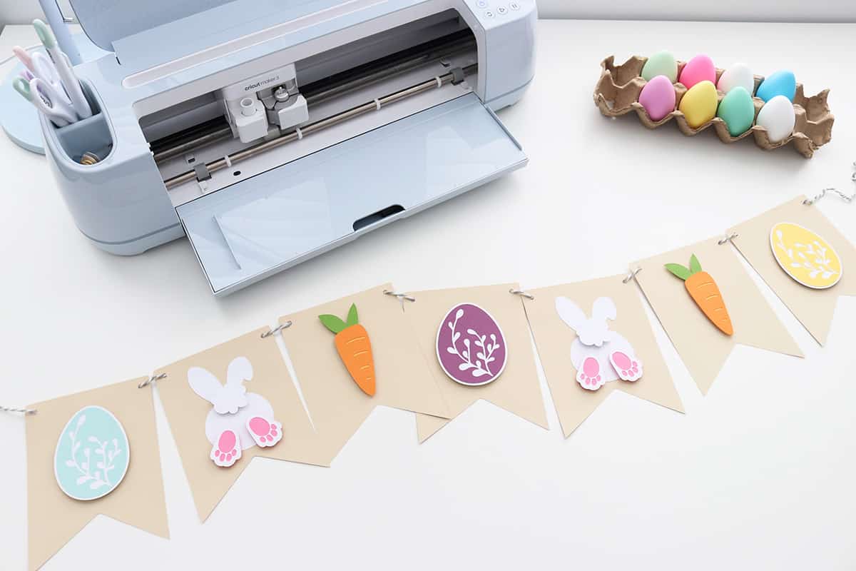 diy easter banner laying on table next to Cricut machine and easter eggs, diy banner tutorial